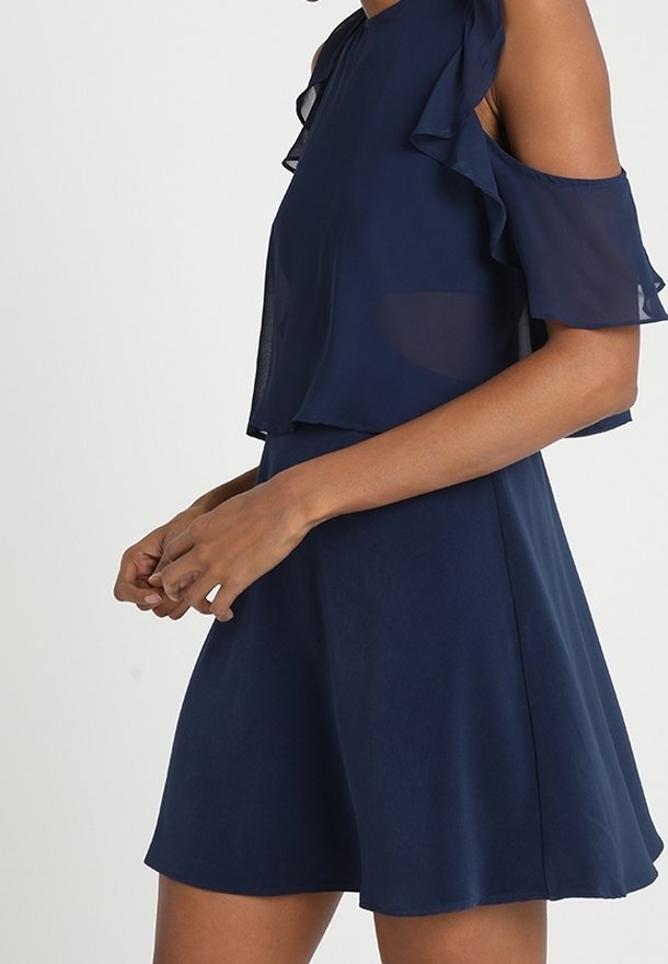 Marinblå klänning med off-shoulder volangärmar, lätt tyg och en flytande kjol som vidgar sig vid nederkanten.