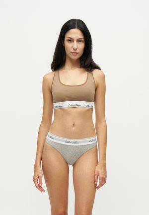 Frau, die nach vorne steht, trägt einen beige-farbenen Sport-BH und graue Unterwäsche mit weißen Calvin Klein Taillenbändern.