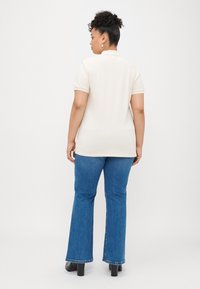 Pólo/bege de mangas curtas, combinado com jeans azuis de perna larga. O conjunto apresenta uma textura suave e um ajuste casual.