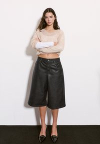 Culotte negre din piele ecologică, cu o tăietură largă, de lungime medie, cu buzunare frontale și închidere cu nasture; asortate cu un pulover ușor de culoare crem.