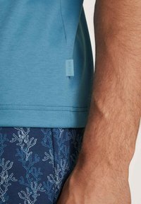 Lichtblauwe katoenen T-shirt, gepresenteerd met een marineblauwe onderkant met een wit koraalpatroon. Inclusief een blauwe labeltag aan de zijkant.