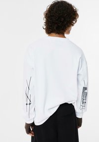 Weißes Langarmshirt mit schwarzen Grafiken auf den Ärmeln, lässige Passform, runder Ausschnitt und weichem Baumwollmaterial.