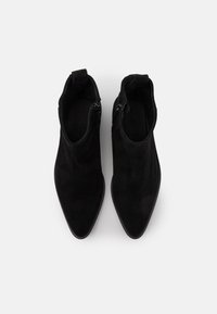 Stivaletti neri in suede alla caviglia con punte appuntite e cerniere laterali. Presentano cuciture minime e un rivestimento interno testurizzato.