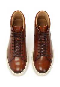 Zapatillas altas de cuero marrón con textura suave, puntera redondeada, cordones marrones y suela de goma blanca. La marca es visible en la lengüeta.
