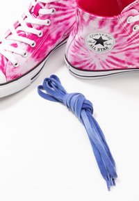 Pink tie-dye canvas high-top sneakers with white laces and a black emblem. A knotted blue shoelace sits beside the shoes.