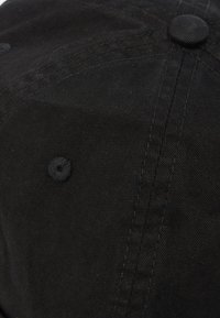 Κοντινό πλάνο ενός μαύρου υφασμάτινου καπέλου μπέιζμπολ που δείχνει ραμμένα πάνελ και οπές αερισμού στην κορυφή.