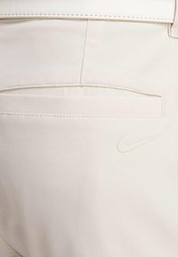 Gaišbeige bikses ar diagonālu žakarda rakstu, aizmugurējo kabatu un mazu, baltu Nike logotipu labajā pusē.