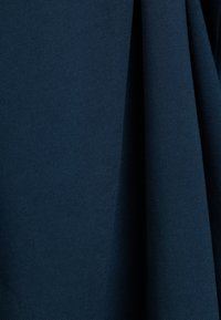 Donkerblauwe geweven stof met een textuur oppervlak, met een lichte glans. Het materiaal hangt zacht met zichtbare plooien en kreuken.