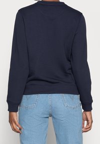 Granatowa bluza z okrągłym dekoltem, długimi rękawami i ściągaczami na mankietach, zestawiona z jasnoniebieskimi dżinsami z kontrastowymi przeszyciami.