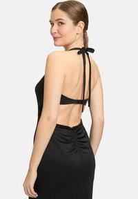 Schwarzes Kleid mit Halterneck. Es verfügt über einen Rückengurt, Raffung in der Taille und mit Perlen besetzte Akzente entlang des Ausschnitts. Glattes Material.
