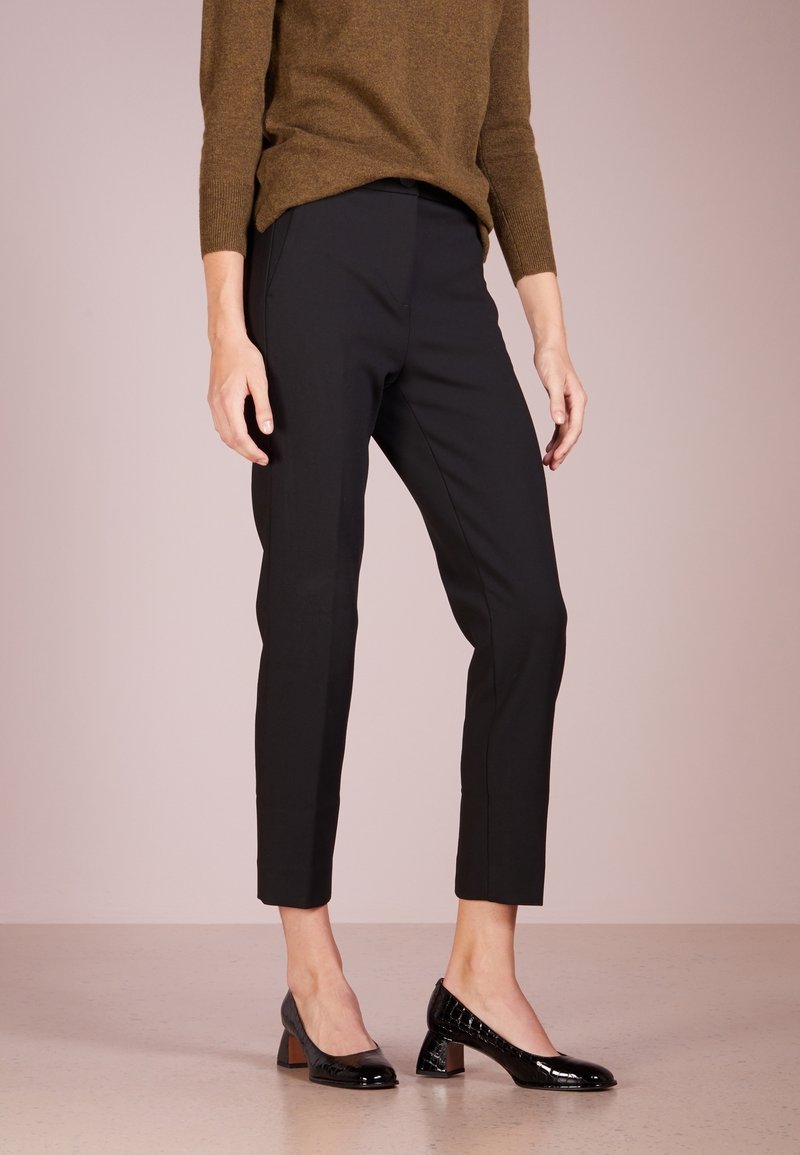 Pantalon noir sur mesure, coupe slim et longueur raccourcie, assorti à des escarpins noirs en cuir verni avec un talon bloc.