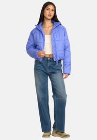Licht paarse pufferjack met een cropped ontwerp, ritssluiting en elastische zoom, gecombineerd met blauwe wijde spijkerbroeken en beige schoenen.