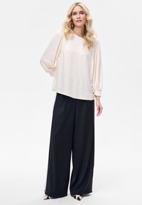 Kremowa bluzka z marszczonymi rękawami, w zestawie z luźnymi czarnymi spodniami z bocznym paskiem i akcentami zwierzęcego wzoru na butach.