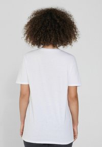 Camiseta de algodón blanca con mangas cortas y cuello redondo, con una textura suave y un corte relajado, vista desde la espalda.