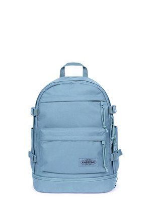 Mochila Eastpak azul clara con bolsillos delanteros y laterales, correas ajustables y una asa superior sobre un fondo blanco.