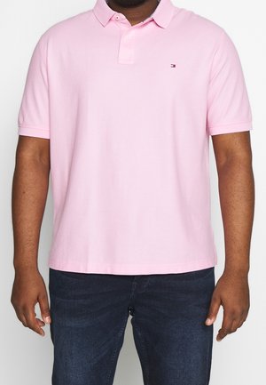 Rosa Baumwoll-Poloshirt mit umgeschlagenem Kragen, kurzen Ärmeln und kleinem Logo. Kombiniert mit dunkelblauen Jeans.