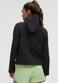Musthave musta sportlik jakk, fiteeritud kapuutsiga disainiga, valmistatud siledast ja paindlikust materjalist. Omab pikki varrukaid ja tõmbluku kaudu reguleeritavat vööd.