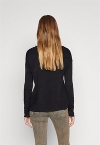 Zwarte trui met lange mouwen, van gestructureerd breimateriaal en een losse pasvorm, gecombineerd met lichtbruine jeans. Zichtbare stiknaden aan de randen.