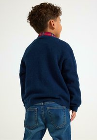 Navyblauer Pullover aus weichem Strickmaterial mit Rundhalsausschnitt und überschnittenen Schultern, kombiniert mit klassischen blauen Jeans.