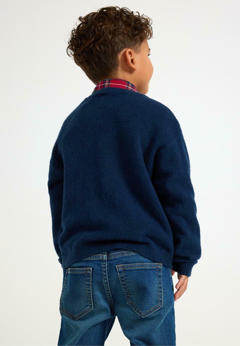Navyblauer Pullover aus weichem Strickmaterial mit Rundhalsausschnitt und überschnittenen Schultern, kombiniert mit klassischen blauen Jeans.