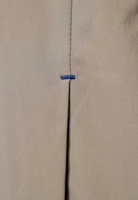 Beige fabric with a visible seam and a single blue stitch accentuating the fold. Smooth texture, detailed stitching along the edge.