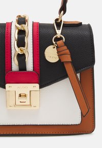 Černá, bílá, hnědá a červená kožená kabelka se zlatým řetízkem, zlatým zámkem s rytinou "ALDO" a hnědým popruhem se zlatým kroužkem a visačkou.