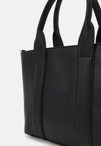 Black leather tote bag with textured surface, dual sturdy handles, and minimalistic design, featuring vertical stitching accents.