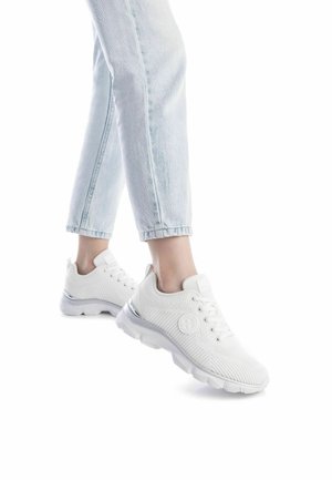 Zapatillas de punto blancas con una parte superior texturizada, cierre de cordones en la parte delantera y un acento de talón de plástico transparente; combinadas con jeans azul claro con vuelta.