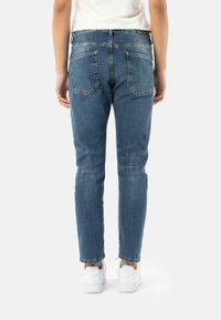 Jean en denim bleu avec une coupe slim, dotés de poches arrière et d'un léger délavage. Associés à des baskets blanches, montrés de l'arrière.