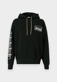 Mustapaita, jossa on valkoiset ja punaiset nyöritykset, "Aries"-logo rinnassa ja toistuva "Aries"-teksti pystysuoralla designilla vasemmassa hihassa.