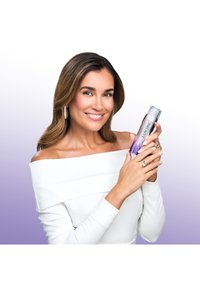 Paarse verloopachtergrond; een vrouw in een wit topje met blote schouders houdt een Lancôme-serumflesje met een zilveren dop vast, waarin het strakke ontwerp wordt getoond.