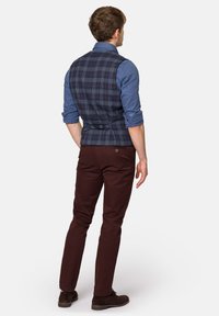 Granatowa kamizelka w kratę o dopasowanym kroju, zestawiona z niebieską koszulą, bordowymi spodniami i brązowymi zamszowymi butami. Kamizelka posiada tylni pasek regulacyjny.