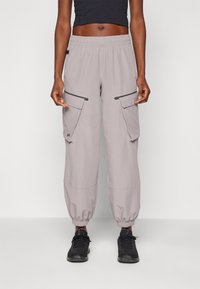 Pantaloni cargo grigio chiaro con polsini elasticizzati, dotati di due tasche laterali e vita regolabile con cordoncino. Il materiale sembra leggero e traspirante.