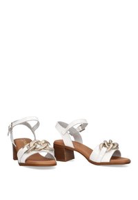 Sandalias de cuero blanco con un bajo tacón cuadrado, que cuentan con un acento decorativo de cadena dorada y correas en el tobillo para mayor soporte. Textura suave.