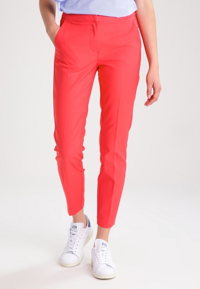 Pantalons rouges ajustés avec une texture lisse et des jambes droites, associés à des baskets blanches. La taille se situe à la taille naturelle.
