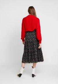 Röd stickad tröja med långa ärmar, kombinerad med en svart blommig kjol. Tillbehören inkluderar vita cowboystövlar med klack.