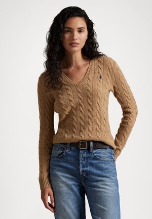 Maglione a maglia cable in tonalità beige con scollatura a V; presenta polsini e orlo a coste. Abbinato a jeans blu e una cintura nera, mostra un look informale.