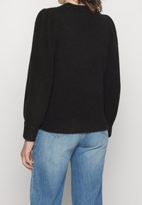 Svart, texturerad tröja med rundad halsringning, åtsittande muddar och en något kortad nederkant, tillsammans med ljusblå denimjeans.