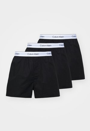 Troje čiernych bavlnených boxeriek s elastickým bielym pásom, na ktorom je značka "Calvin Klein". Boxerky majú voľný strih a žiadne ďalšie vzory.