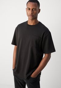 Sort bomulds T-shirt med korte ærmer, rund hals og brystlomme. Glat tekstur, afslappet pasform, minimalistisk design.