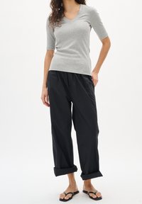 Grå ribbad kortärmad V-ringad topp kombinerad med svarta löst sittande byxor, uppvikta benslut, och svarta flip-flops. Enfärgad bakgrund.