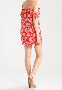 Vestido floral rojo con flores blancas, diseño sin hombros, mangas con volantes, tejido ligero, largo por encima de la rodilla, combinado con tacones beige.