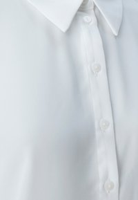 Camicia bianca con una texture liscia, colletto classico e apertura frontale con bottoni trasparenti, caratterizzata da un design minimalista.