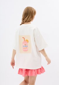Witte oversized t-shirt met een grafiek van een roze drankje met de tekst "ALOHA." Rimpelige roze zoom voegt detail toe. Soepele textuur, casual ontwerp.