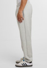 Hellgraue Sweatpants mit einem elastischen Bund, Seiten pockets und einem schmal zulaufenden Bein Design, getragen mit weißen und schwarzen Turnschuhen.