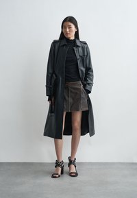 Must mustrõngast ja kintsuvöödiga must nahkne trench coat, millele on kokku sobitatud pruun nahkseelik. Omab kõrgete kontsadega musti sandaale ringjate aktsentidega.