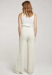 Pantalon large en tissu beige doux et pâle avec une finition texturée. Design taille haute, comportant des coutures minimalistes et des fentes latérales.