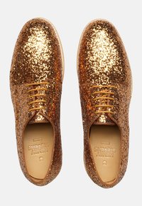 Sneaker di glitter oro con una texture liscia, presentano una punta rotonda, allacciatura frontale e un branding discreto sulla suola interna.