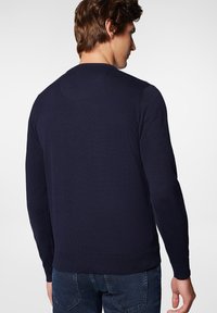 Granatowy sweter dzianinowy z długimi rękawami, ribbowanymi mankietami i dołem; okrągły detal yoke z tyłu. Materiał wydaje się gładki i dopasowany.