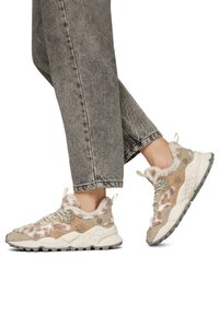Fuzzy beige sneakers with light gray accents, floral design elements, thick soles, and textured fabric. Paired with light gray jeans.